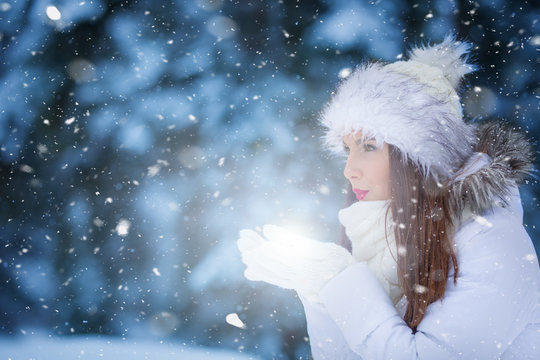 Attractive young woman blowing snow in snowy night