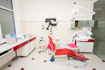 Dentist office with red dentist chair and dental equipment including microscope, healozone device and endodontic unit