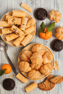 Waffles tubules and profiteroles on a rustic background. Chocolate biscuits and tangerines on a wooden light background.