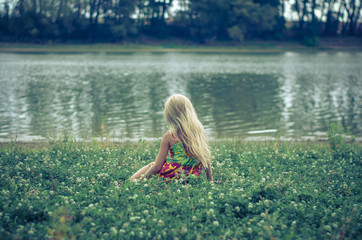little lonely girl sitting in the grass by the river