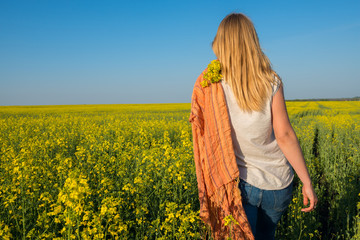 Young woman blonde is walking across the field of yellow flowers