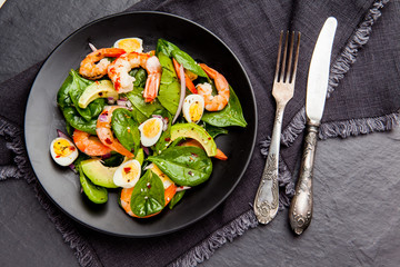 Fresh, healthy salad with shrimps, spinach and avocado on a black background. Top view
