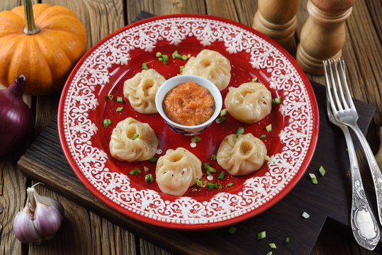 Traditional Asian food. Nepalese dumplings momo with curry sauce served with leek, onion, garlic and pumpkin on bright red plate