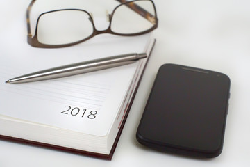 New Year 2018 office organizer calendar, smartphone, glasses and sliver ballpen. Selective focus