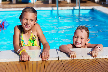 Little children playing and having fun in swimming pool with air mattress. Kids playing in water. Swimming concept. Boy and girl swim in resort pool during vacations