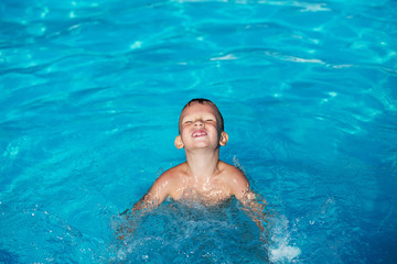 Happy kid playing in blue water of swimming pool. Little boy learning to swim. Summer vacations concept. Cute boy swimming in pool water. Child splashing in swimming pool