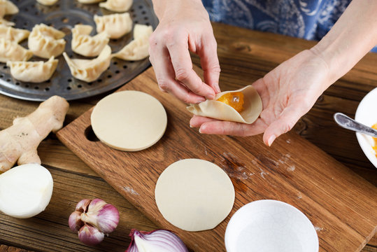 Closeup of woman hands stuffing steam dumplings with pumpkin on rustic wooden background