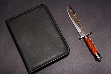 Hunting knife on a black background with leather folder.