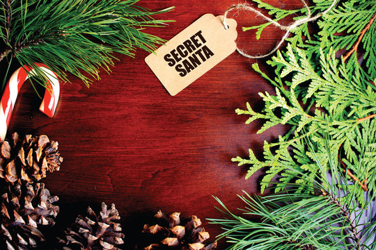 Secret Santa background with tag, festive branches, pine cones and candy cane.