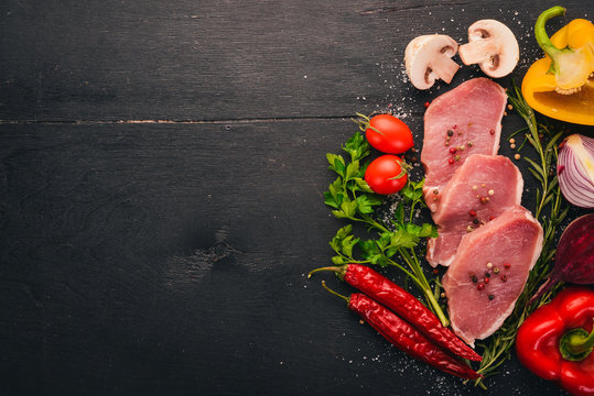 Beef steak with fresh vegetables and rosemary and spices on a black wooden background. Top view. Free space for text.