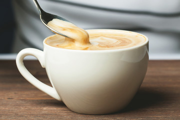 A cup and foam cappuccino, raised spoon.