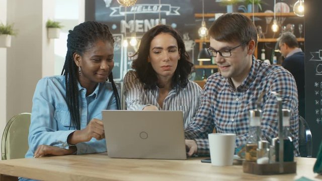 Three Young People in the Coffee Shop, They Work on a Laptop and Talk. In the Background Stylish Cafe Establishment.  Shot on RED EPIC-W 8K Helium Cinema Camera.