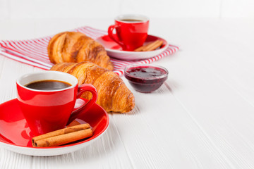 Freshly baked croissant on napkin, cup of coffee in red cup on white wooden background. French breakfast. Fresh pastries for breakfast. Delicious dessert. Closeup photography. Horizontal banner