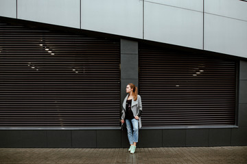 Fototapeta na wymiar Concept of street fashion. An autumn portrait of the nice young smiling girl against the background of an impressive gray wall. Beautiful model in the city in a gray coat, blue jeans and a warm color 