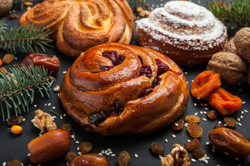Christmas tree with decoration on a black background. Traditional homemade buns with powdered sugar and dried fruits.