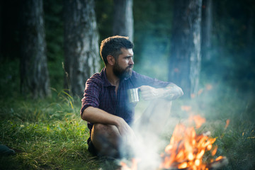 Hipster hiker with mug relax at bonfire in forest