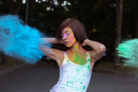Lovely brunette woman with short hair posing with exploding Holi blue and green paint