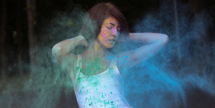 Gorgeous young woman with short hair posing with exploding Holi blue and green dry paint