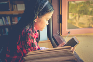 Girl is using tablet while sitting in library and reading a book