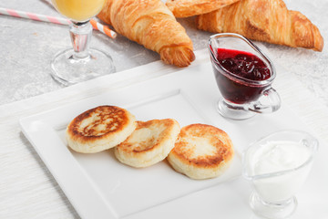 Curd fritters served with sour cream and cherry jam. Breakfast conception with fresh orange juice and baked goods