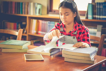 Girl is using tablet while sitting in library and reading a book