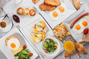 Breakfast table with egg Benedict, fried eggs and sausages, toasts with fried eggs and cheese, curd fritters. Fresh orange juice and coffee with bread rolls and croissants. Top view, flat lay
