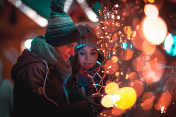 Couple in warm clothes enjoying colorul Christmas market, bokeh lights background