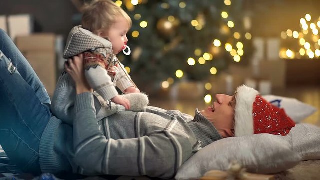 Happy father and adorable newborn baby playing in front of Christmas tree