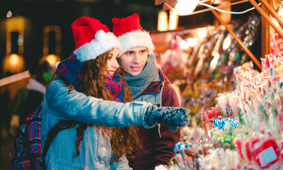 Couple at colorful Christmas market choosing things for buying