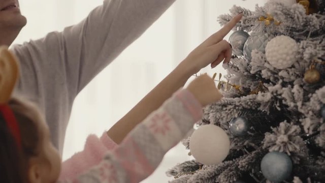 happy young family from mom, dad, and little girl decorate a Christmas tree, slow motion