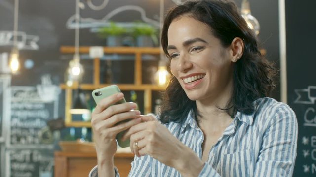 Beautiful Woman Uses Smartphone while Sitting in the Cafe. Background of This Stylish Coffee Shop. Shot on RED EPIC-W 8K Helium Cinema Camera.