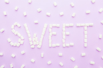 word "sweet" of mini marshmallows on pink  background. Top view