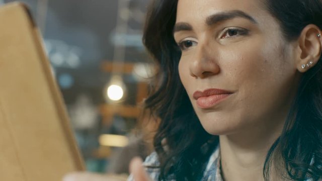Portrait of the Beautiful Hispanic Woman Uses Tablet Computer while Sitting in the Stylish Cafe. Shot on RED EPIC-W 8K Helium Cinema Camera.