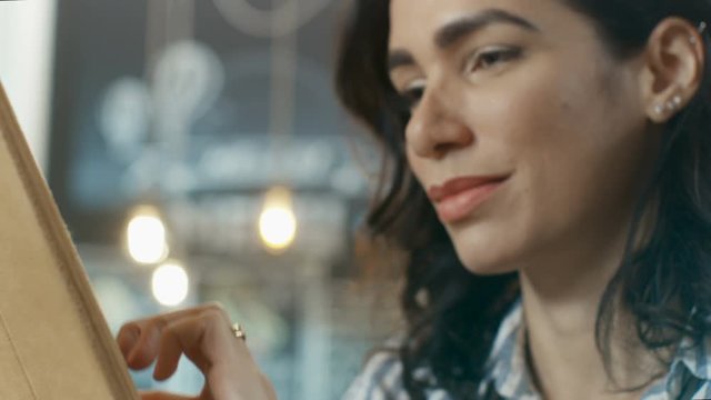 Portrait of the Beautiful Hispanic Woman Uses Tablet Computer while Sitting in the Stylish Cafe. She Makes Swiping Gestures. Shot on RED EPIC-W 8K Helium Cinema Camera.