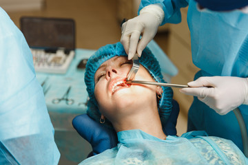 Close up process of male professional dentist surgeon performing operation install dental implant teeth of woman patient in clinic light office with modern tools equipment. Blood and pain on the face.