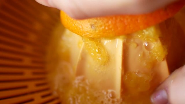 The girl squeezes juice from an orange with a hand-held juicer
