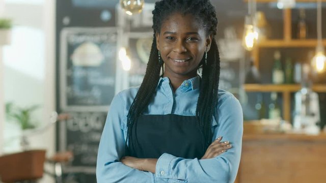 Beautiful African-American Cafe Owner Standing with Crossed Arms and a Smile in Her Stylish Coffee House. Shot on RED EPIC-W 8K Helium Cinema Camera.