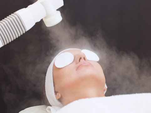 The procedure of steaming the skin of the face of a young woman before cleaning the skin in a cosmetology salon.