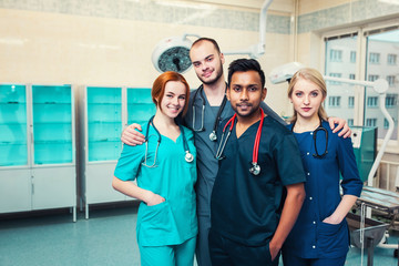 group young multiracial medical students with surgeons hugging each other looking with a smile at the camera. Hospital operating room in the background