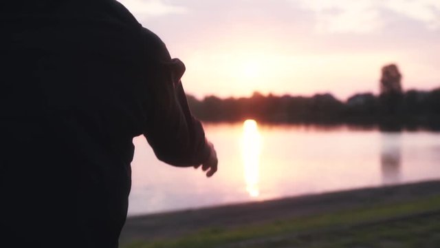 Slow motion man warming up near quiet river. Back view male swinging arms and jumping beautiful morning water panorama.