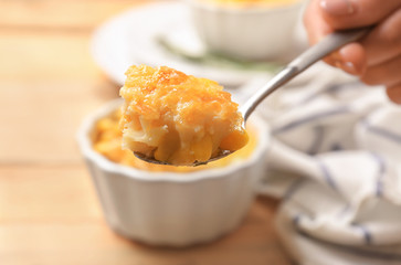 Woman holding spoon with corn pudding on blurred background