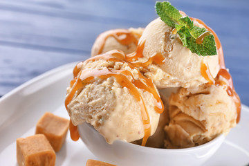 Bowl of delicious ice cream with caramel topping on plate, closeup