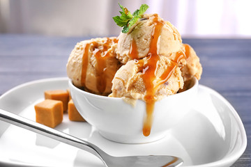 Bowl of delicious ice cream with caramel topping on plate, closeup