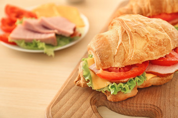 Wooden board with delicious croissant sandwich on table, closeup