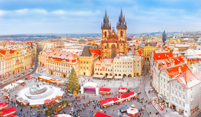 Naklejka premium Praga w czasie świąt Bożego Narodzenia, klasyczny widok na zaśnieżone dachy w centralnej części miasta i jarmark bożonarodzeniowy na starym placu na tle kościoła Tyn. Sezonowy zimowy krajobraz miasta Pragi.