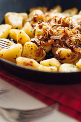 Traditional German fried potatoes, so called Bratkartoffeln, with caramelized, browned onions roasted in a enamel cast iron pan seasoned with caraway, salt, pepper, parsley and chives
