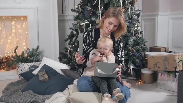 Happy mother and daughter embracing. White fireplace and decorated tree on background. Christmas or New year celebration.