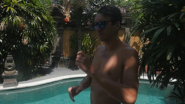 man in sunglasses jumps flip in the pool outdoor at resort in slow motion