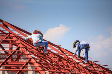 welder workers installing steel frame structure of the house roof at building construction site