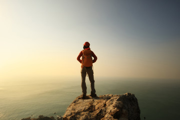 Obraz premium female hiker stand on the cliff edge at sunrise seaside